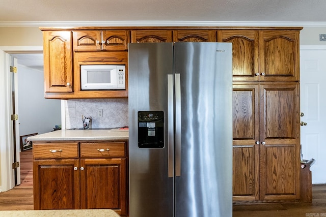 kitchen with tasteful backsplash, stainless steel refrigerator with ice dispenser, ornamental molding, and hardwood / wood-style floors