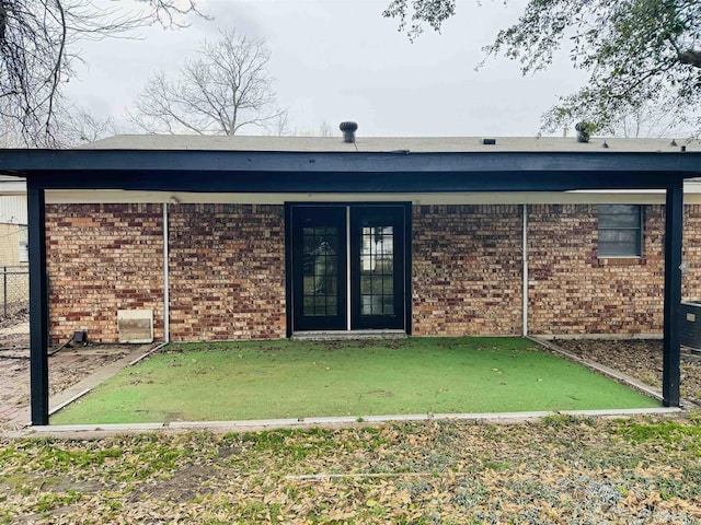 entrance to property with brick siding, a lawn, and fence