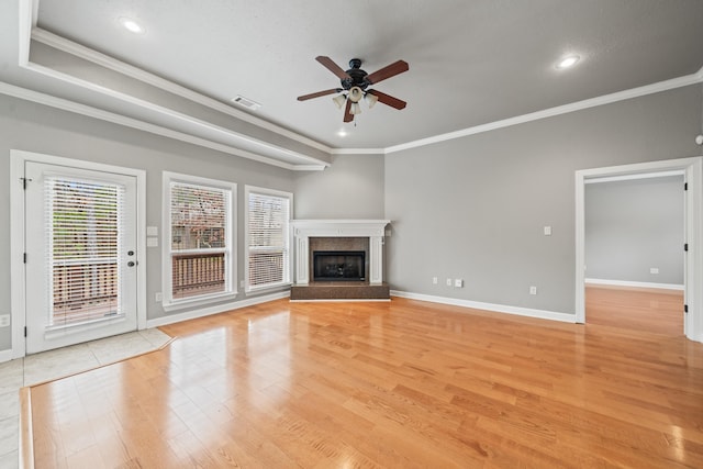 unfurnished living room with crown molding, ceiling fan, light hardwood / wood-style floors, a raised ceiling, and a premium fireplace