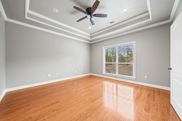 empty room with a raised ceiling, ornamental molding, ceiling fan, and light hardwood / wood-style flooring