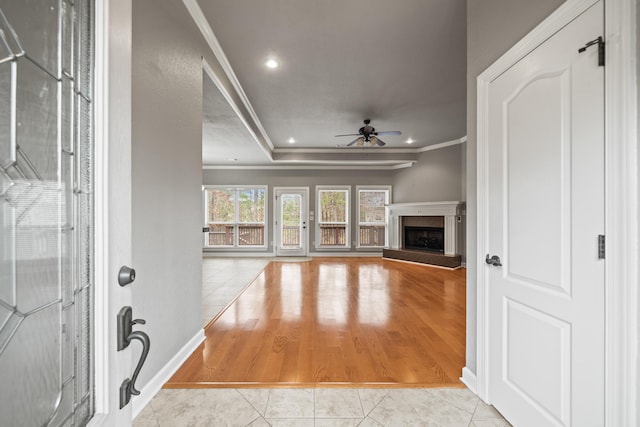 unfurnished living room with light tile patterned floors, crown molding, a raised ceiling, and ceiling fan