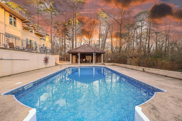 pool at dusk featuring a gazebo and a patio