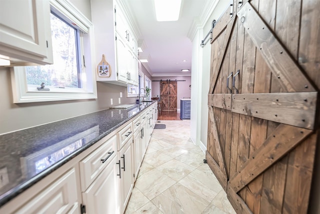 kitchen featuring sink, white cabinets, dark stone counters, ornamental molding, and a barn door