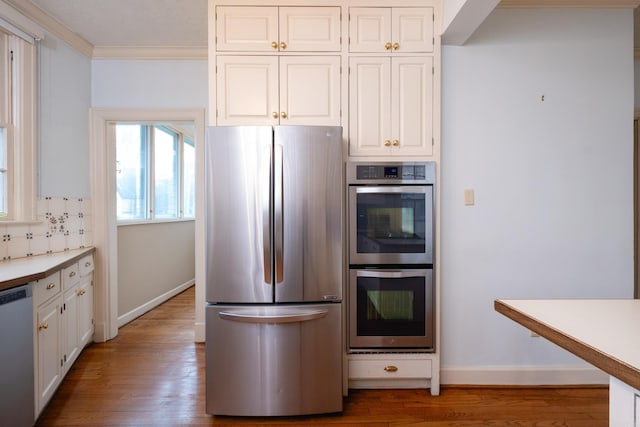 kitchen featuring crown molding, white cabinets, stainless steel appliances, hardwood / wood-style floors, and backsplash