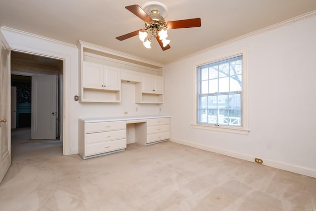 unfurnished office featuring crown molding, ceiling fan, built in desk, and light carpet