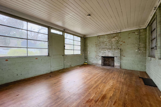 unfurnished living room with brick wall, hardwood / wood-style floors, a stone fireplace, and wood ceiling