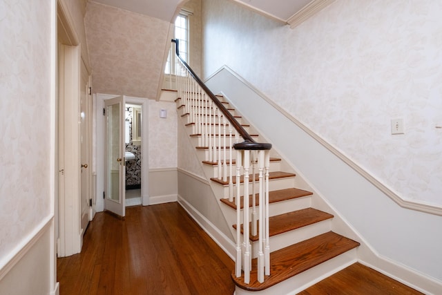 stairway featuring wood-type flooring, a towering ceiling, and crown molding