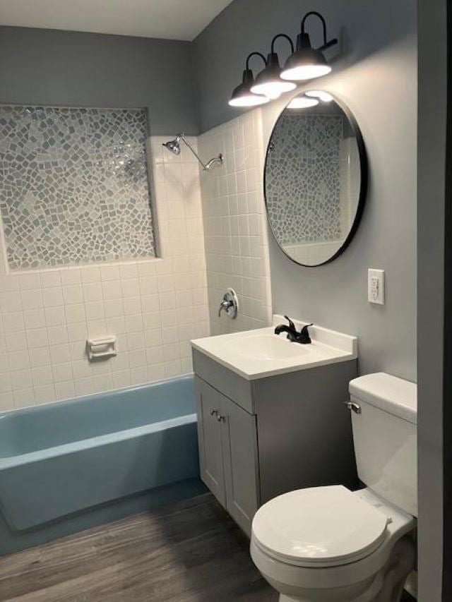 full bathroom with tiled shower / bath, hardwood / wood-style floors, vanity, and toilet