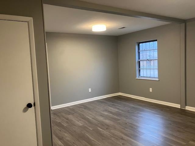 empty room featuring beamed ceiling and dark hardwood / wood-style flooring