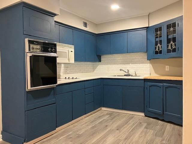 kitchen featuring tasteful backsplash, sink, black appliances, blue cabinetry, and light hardwood / wood-style flooring