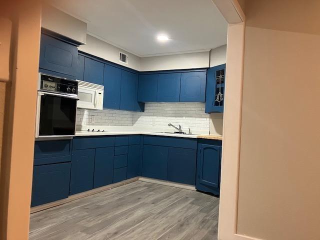 kitchen with sink, light hardwood / wood-style flooring, oven, and blue cabinets