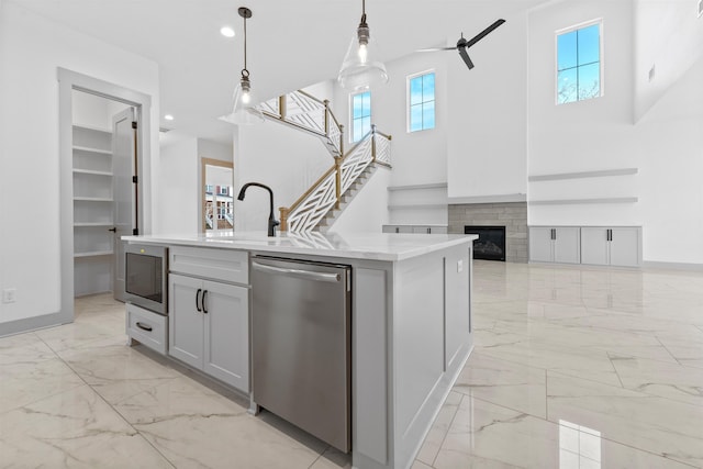 kitchen featuring pendant lighting, sink, a center island with sink, built in microwave, and stainless steel dishwasher