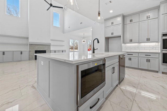 kitchen with sink, a kitchen island with sink, hanging light fixtures, tasteful backsplash, and built in microwave