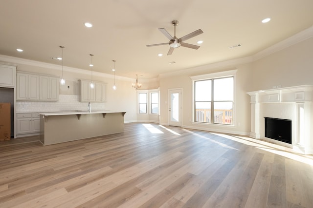 unfurnished living room featuring sink, a premium fireplace, ornamental molding, light hardwood / wood-style floors, and ceiling fan with notable chandelier