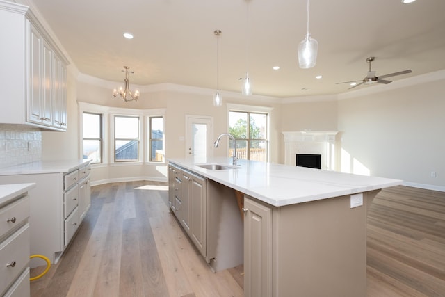 kitchen featuring sink, tasteful backsplash, ornamental molding, a center island with sink, and decorative light fixtures