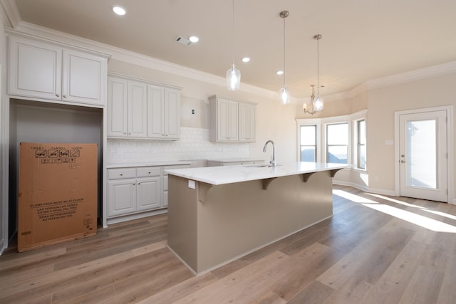 kitchen with a breakfast bar, hanging light fixtures, light stone countertops, an island with sink, and white cabinets