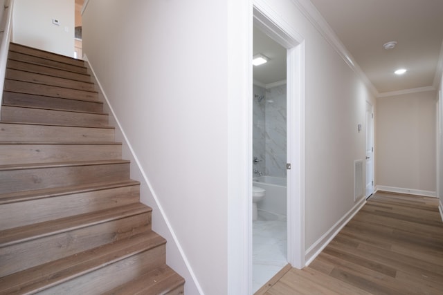 stairway with wood-type flooring and ornamental molding