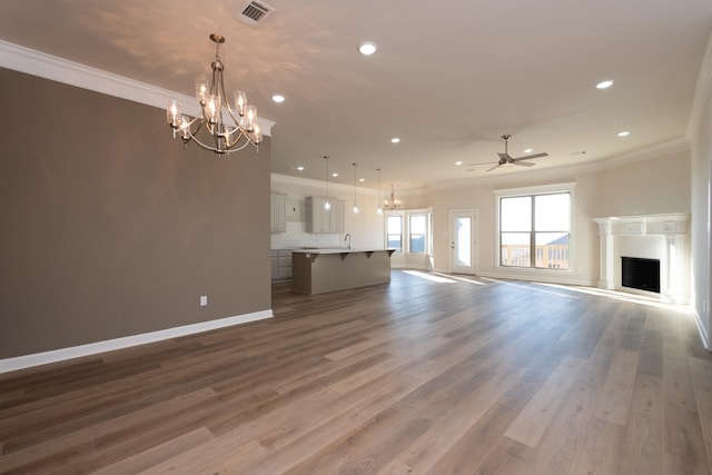 unfurnished living room with ornamental molding, ceiling fan with notable chandelier, and wood-type flooring