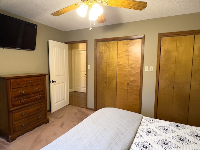 carpeted bedroom featuring ceiling fan, two closets, and a textured ceiling