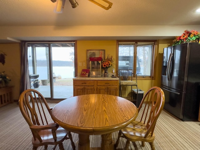 dining space featuring a water view, light carpet, and ceiling fan