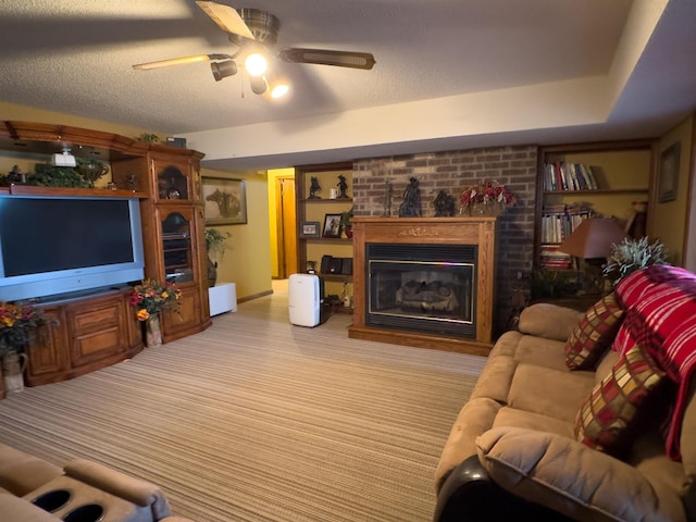 living room with ceiling fan, light colored carpet, a brick fireplace, and a textured ceiling