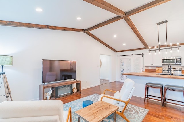 living room featuring vaulted ceiling with beams, light hardwood / wood-style flooring, and a barn door