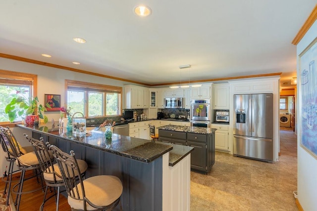 kitchen with pendant lighting, appliances with stainless steel finishes, gray cabinetry, dark stone countertops, and washer / clothes dryer