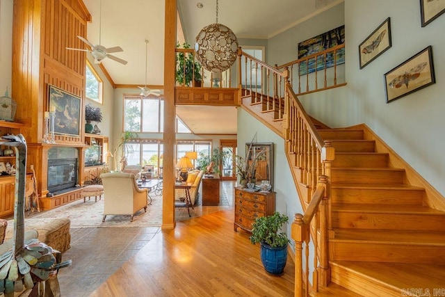 staircase featuring a towering ceiling, wood-type flooring, ornamental molding, and ceiling fan