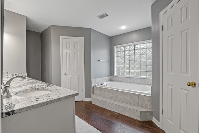 bathroom featuring hardwood / wood-style flooring, vanity, and tiled bath