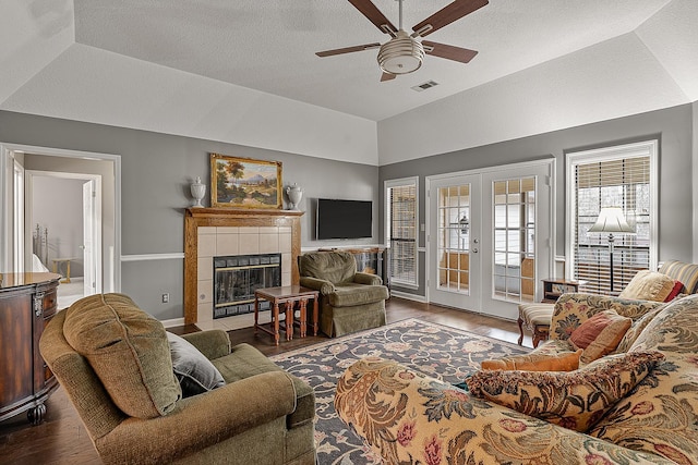 living room with french doors, vaulted ceiling, dark hardwood / wood-style flooring, a tile fireplace, and ceiling fan