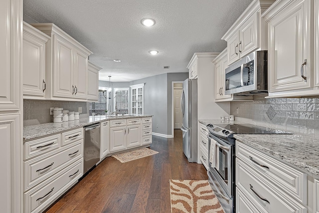 kitchen with appliances with stainless steel finishes, dark hardwood / wood-style floors, light stone counters, white cabinets, and decorative light fixtures