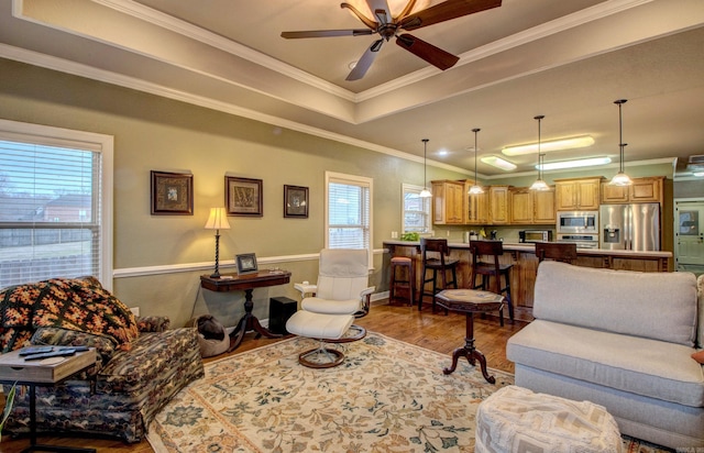 living room with a tray ceiling, ornamental molding, ceiling fan, and light wood-type flooring