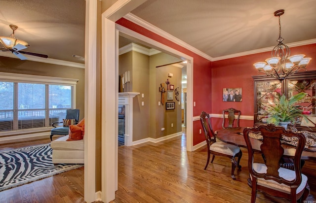 dining space featuring hardwood / wood-style flooring, a fireplace, ceiling fan with notable chandelier, and crown molding