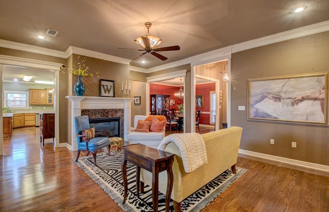 living room with ceiling fan, wood-type flooring, a premium fireplace, and ornamental molding