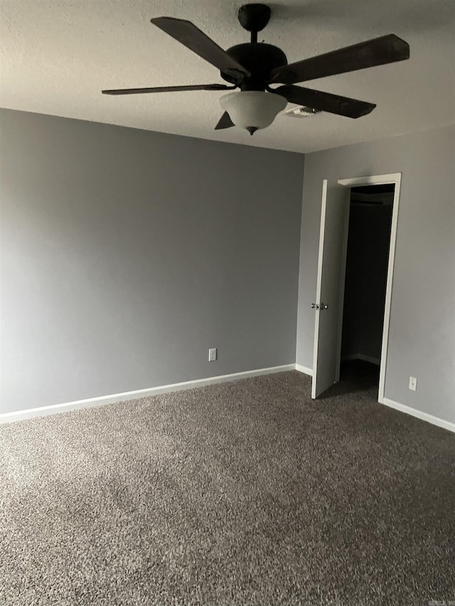 empty room with a textured ceiling, ceiling fan, and dark colored carpet