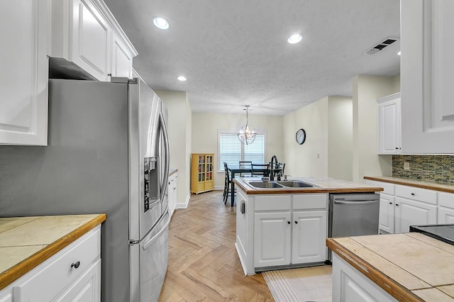 kitchen with sink, appliances with stainless steel finishes, white cabinetry, hanging light fixtures, and tile countertops