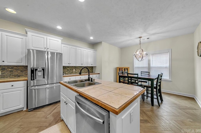 kitchen featuring white cabinetry, decorative light fixtures, tile counters, an island with sink, and stainless steel appliances