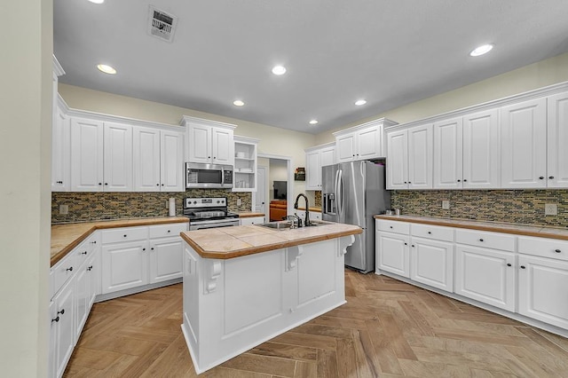 kitchen with appliances with stainless steel finishes, white cabinetry, an island with sink, sink, and tile counters