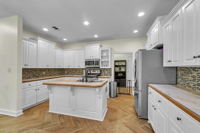 kitchen featuring tile countertops, stainless steel appliances, white cabinets, and a center island with sink