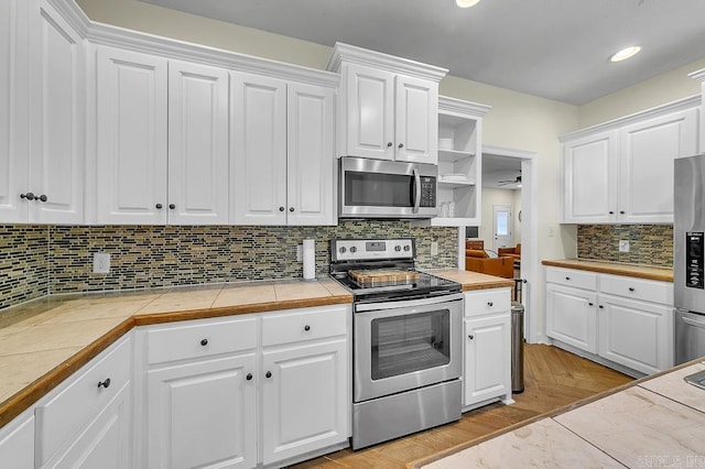 kitchen featuring light hardwood / wood-style flooring, appliances with stainless steel finishes, white cabinetry, tasteful backsplash, and tile counters