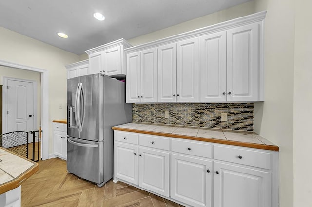 kitchen featuring backsplash, tile counters, stainless steel fridge, and white cabinets