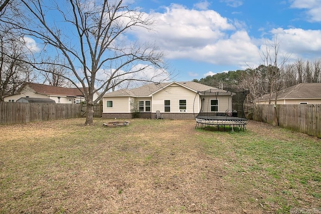 rear view of house with a yard, a trampoline, and a fire pit