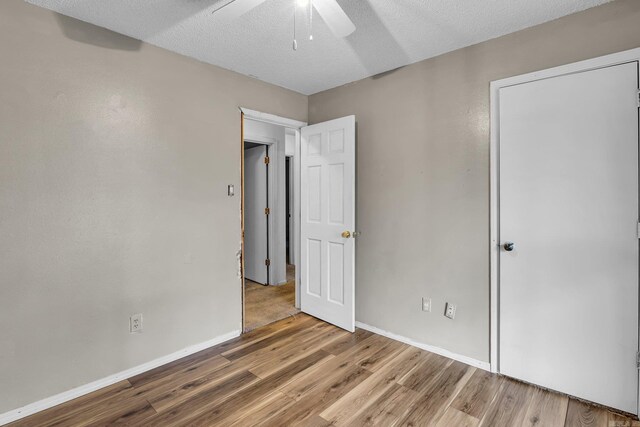 unfurnished bedroom featuring a ceiling fan, a textured ceiling, baseboards, and wood finished floors