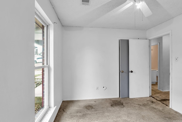 carpeted spare room featuring a ceiling fan, visible vents, plenty of natural light, and a textured ceiling