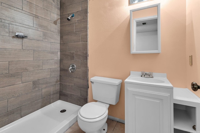 bathroom featuring toilet, baseboards, tiled shower, and vanity