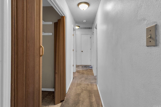 corridor featuring carpet, baseboards, a textured ceiling, and a textured wall