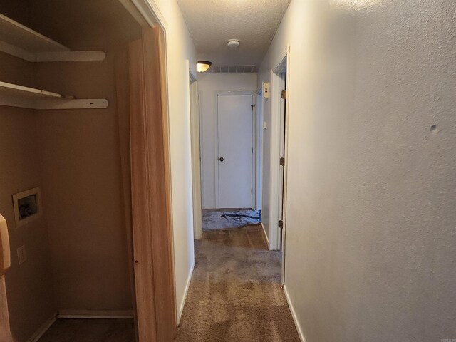 hall featuring a textured ceiling, carpet flooring, visible vents, and baseboards