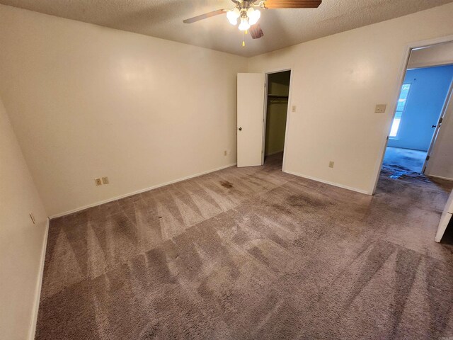 unfurnished bedroom with baseboards, ceiling fan, a spacious closet, a textured ceiling, and carpet flooring