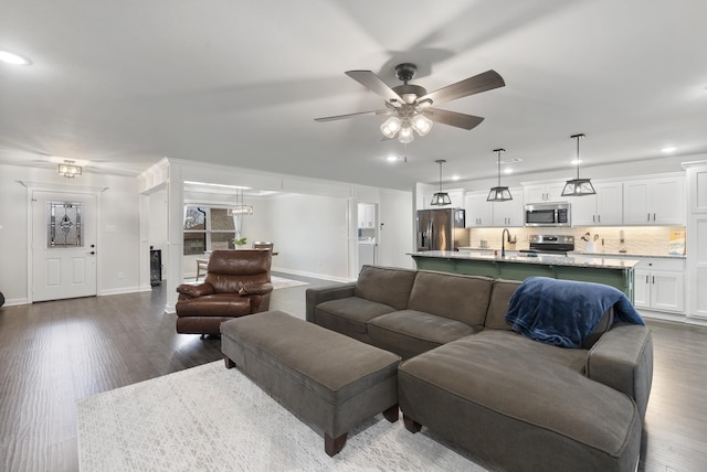 living room featuring dark hardwood / wood-style flooring, sink, and ceiling fan with notable chandelier