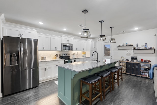 kitchen featuring appliances with stainless steel finishes, decorative light fixtures, white cabinetry, light stone countertops, and a center island with sink